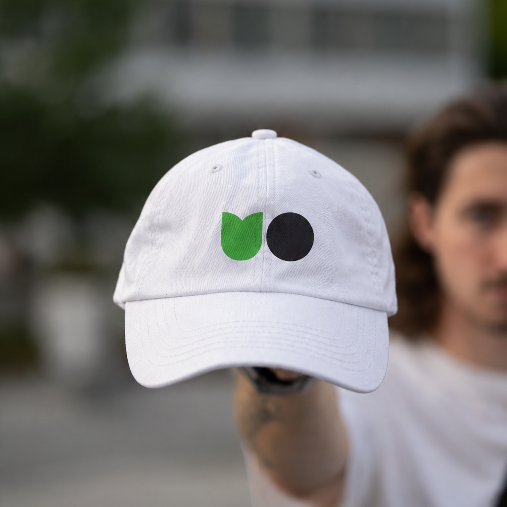 A white cap with the Urban Optimists logo held towards the camera